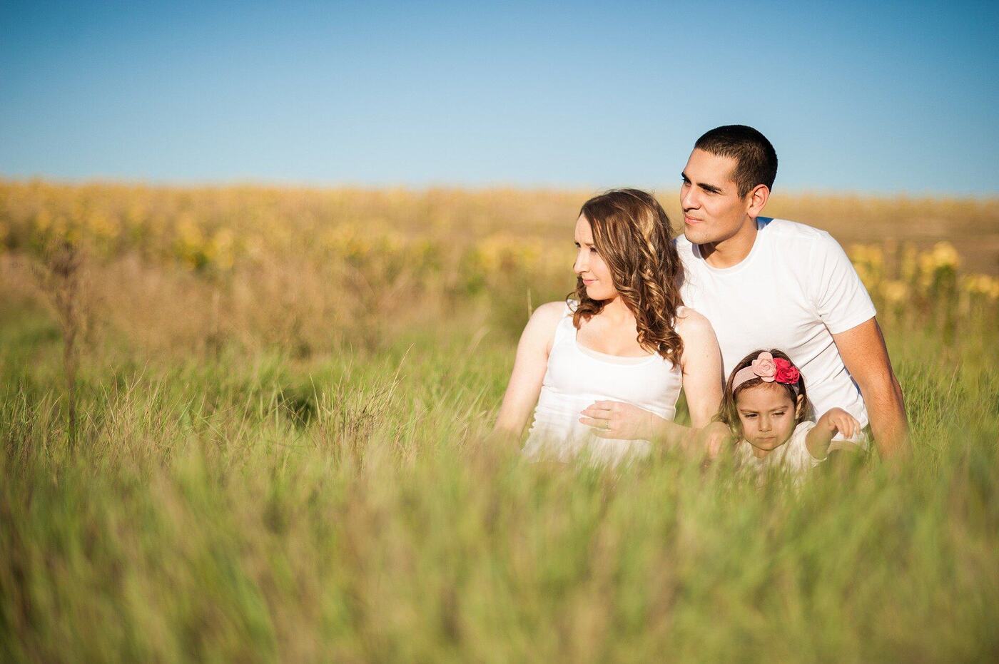 A mother, father and young daughter sitting together in a grassy field